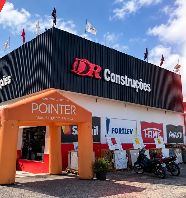 Fachada da DR Construções em Delmiro Gouveia com bandeiras no topo e placas de marcas parceiras